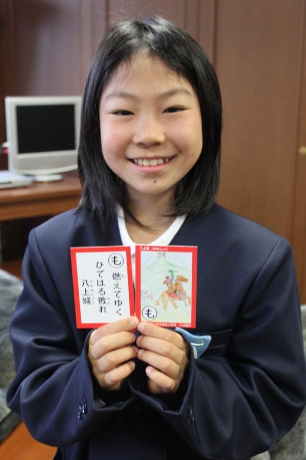 優秀賞を受賞した「も」の読み札と取り札を両手に持ち笑顔の小林優希さんの写真